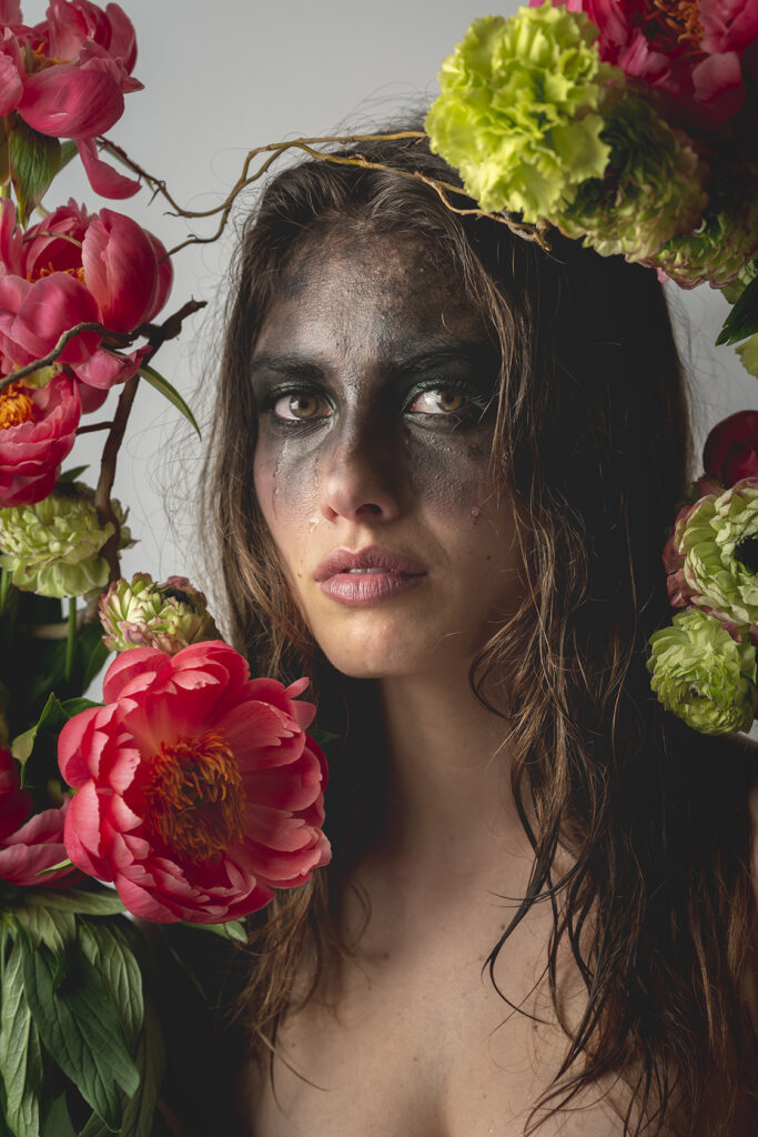 Stefano Delìa – La Scala di Mohs, fotografia n.6 Stefano Delìa, fotografia autoriale dal progetto La Scala di Mohs, scatto n.6 con ritratto femminile, volto segnato da trucco nero e lacrime, incorniciato da fiori