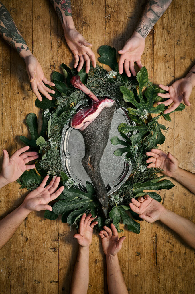 Se carne questa carne Opera fotografica Celebrazione di Stefano Delìa per la cena performance Se Carne, Questa Carne, mani che circondano una zampa di animale su vassoio con foglie