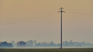 Paesaggio rurale nella nebbia, Pianura Padana – fotografia di Stefano Delia Campo della Pianura Padana con traliccio e cascina immersi nella nebbia al tramonto