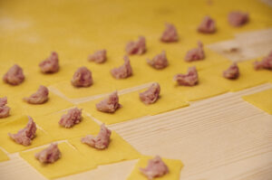 Pasta fresca con ripieno per tortellini emiliani Sfoglia di pasta fresca tagliata a quadrati con ripieno di carne per tortellini tradizionali emiliani