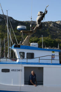 Peschereccio Adele con marinaio | Most of Italy | Foto Stefano Delìa Peschereccio Adele nel porto con marinaio a bordo e un orso di peluche fissato sull’albero maestro, fotografia documentaria di Stefano Delìa per Most of Italy