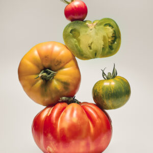 Pomodori di diverse varietà e colori disposti in equilibrio su fondo neutro, fotografia fine art food