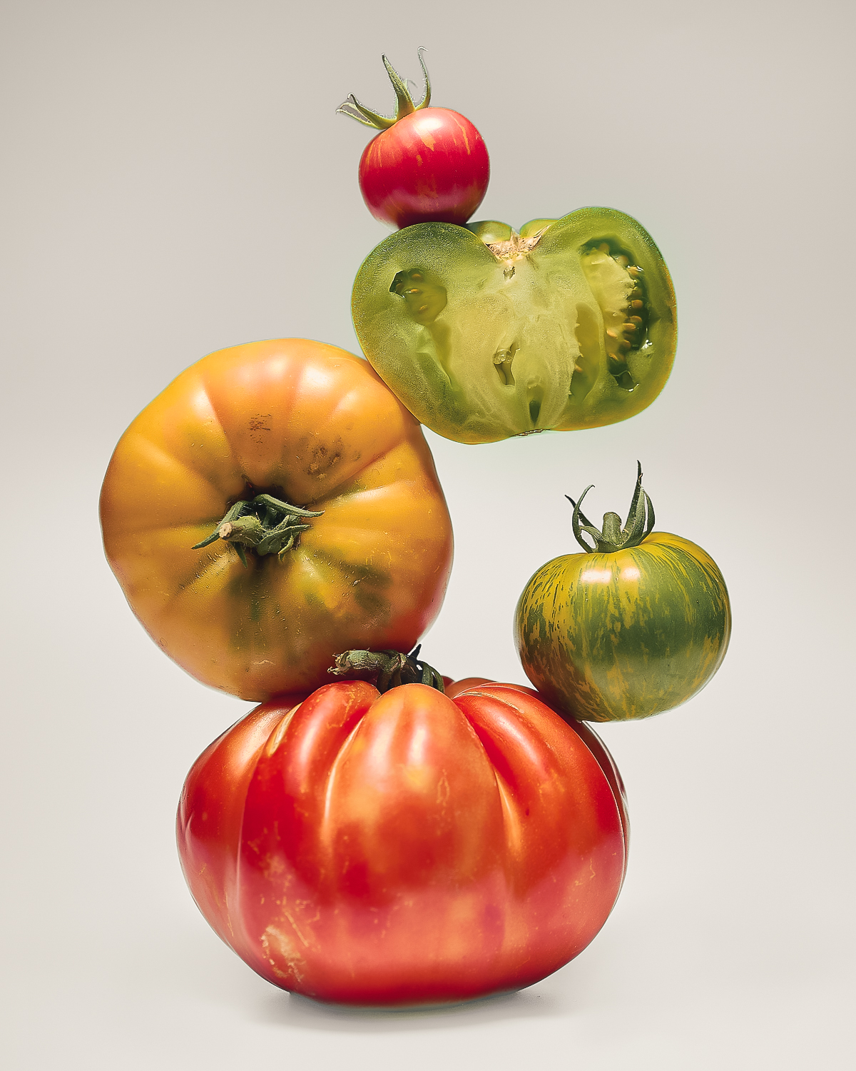 Pomodori di diverse varietà e colori disposti in equilibrio su fondo neutro, fotografia fine art food