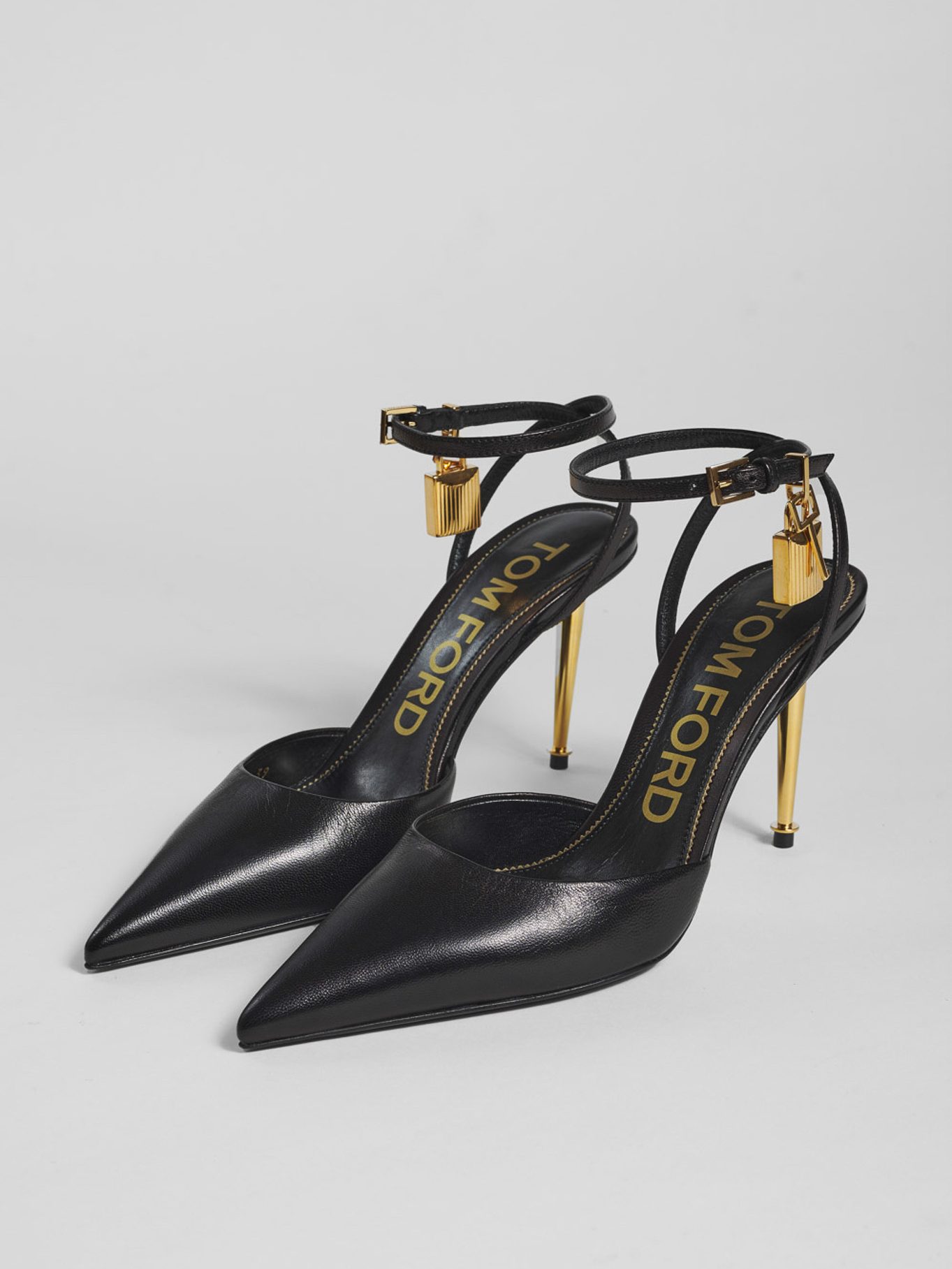 Décolleté slingback Tom Ford in pelle nera con tacco e lucchetto dorati, still life di prodotto su fondo grigio neutro